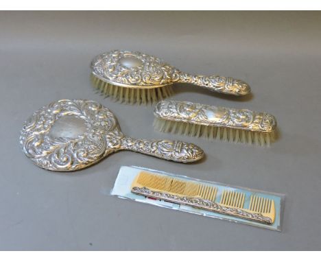 A silver four piece dressing table set, comprising a hand mirror, hair brush, clothes brush, and comb