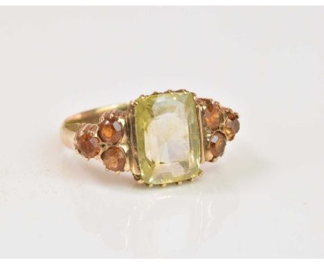 A yellow metal dress ring with pale green coloured central stone and orange stones to the shoulders, size L, approx 3.73g.