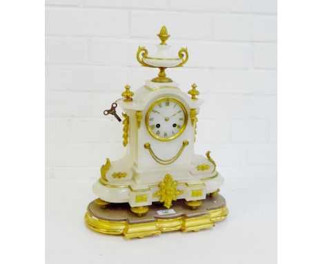 A white hardstone and ormolu mantle clock, the arched top surmounted by a twin handled urn with acorn finial, the circular di