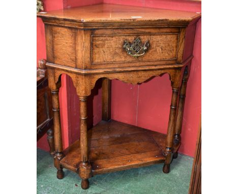 An oak corner side table, moulded top above a single frieze drawer, brass handle and escutcheon, spreading cylindrical suppor