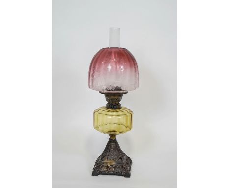 A glass and iron oil lamp with a cranberry shade, highlighted with acid etched decoration over a clear yellow glass reservoir