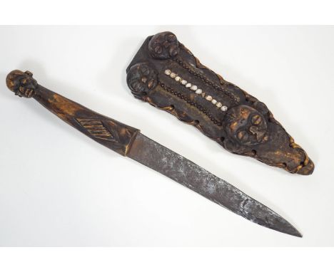 A Congolese knife, in wood and iron, the handle with a male mask finial, in a wood scabbard decorated with three similar moti