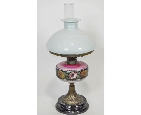 An opaline glass and brass oil lamp with a white glass shade over a graduated pink reservoir, decorated with a floral band on
