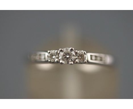 A white metal three stone diamond ring with diamond set shoulders. Hallmarked 9ct gold, Edinburgh. Supplied with original pur