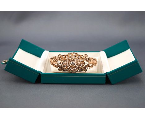 A rose metal hinged bangle having a large floral cluster design set with old rose cut and macle cut diamonds. Hinged fitting 