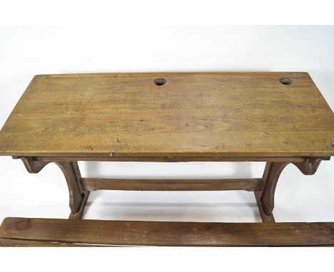 A child's double school desk, the sloping top with two recesses for inkwells, with attached bench seat, 80cm high x 120cm lon