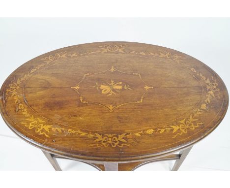 An Edwardian mahogany side table, the oval top in satin and coloured woods, inlaid with a central musical trophy in a floral 