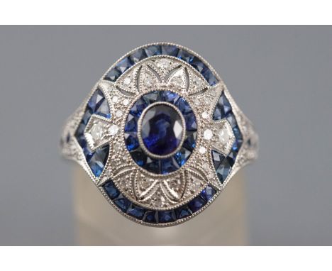 A white metal dress ring principally set with an oval faceted cut blue sapphire measuring approximately 5.00mm x 4.00mm. Furt