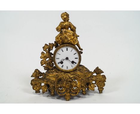 A cast gilt metal French clock, of Rococo form with white Roman dial topped with a figure of a girl playing a hurdy gurdy, th