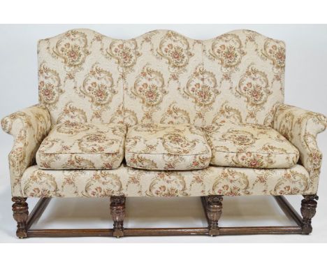 A Jacobean style three seater sofa with domed back over scrolled arms and loose cushions raised on a stretchered oak base wit