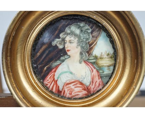A portrait miniature of a lady sat in a columned arcade looking out to a park with a mansion, in a round gilt frame, 9.5cm di