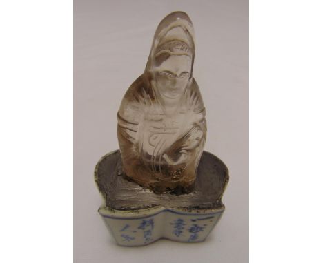 An oriental carved rock crystal figurine paperweight mounted on a shaped blue and white ceramic plinth, 11.5cm (h)