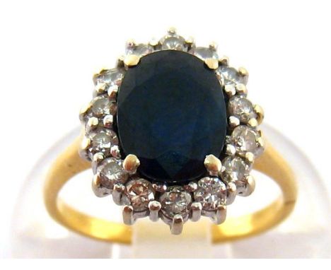 A sapphire and diamond cluster ring, the central oval cut stone 8.2 x 6.1mm, in a surround of small brilliants, the yellow me