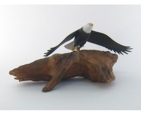 A carved and painted wood sculpture of an eagle, wings outstretched, flying above a stripped natural wood form representing a