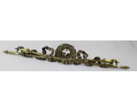 A decorative brass finial centred with a wreath and flanked by crossed spears and ribbon, width 70cm, height 11cm. 