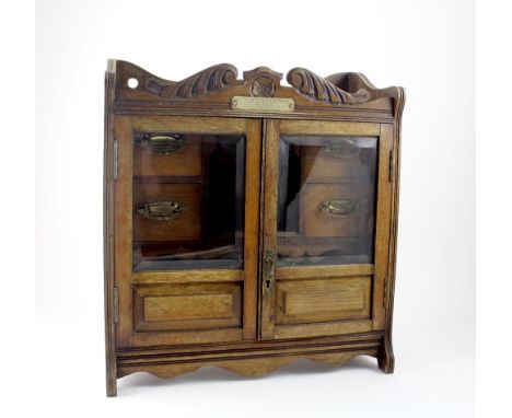 An oak smoker's cabinet, two half-glazed doors with four small drawers and pipe stands to interior, with brass detailed handl