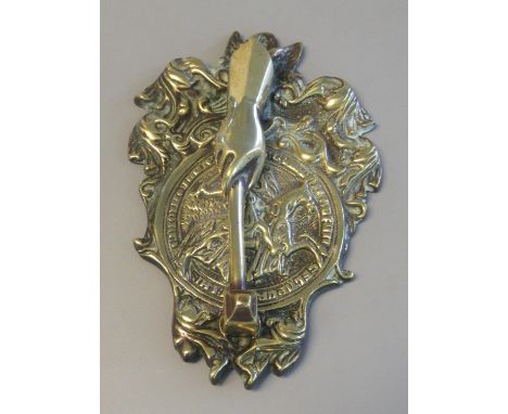 Heavy door knocker with relief brass back plate featuring mounted knight amid scroll work, with the hammer in the form of a b