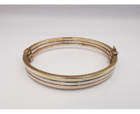 A modern 9ct three colour gold hinged bangle. The bangle comprised of three bands, white, rose and yellow gold. Fastens with 