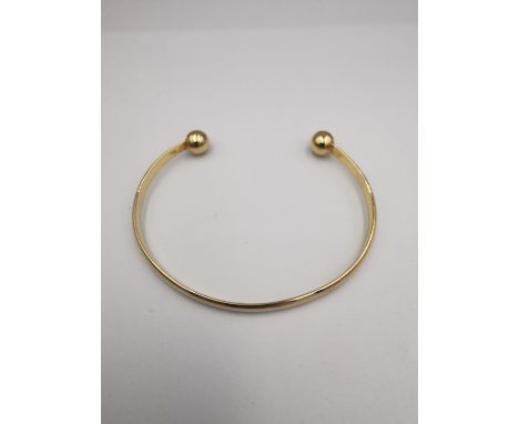 A 9ct yellow gold D-shaped bangle with ball ends. Hallmarked for 9ct. Weight.11.42g Dia.7cm 