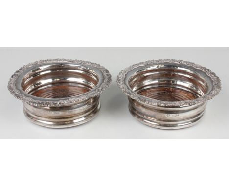 A pair of George V silver wine coasters, each with cast foliate and scroll rim and turned wooden base, Sheffield 1911 by Will
