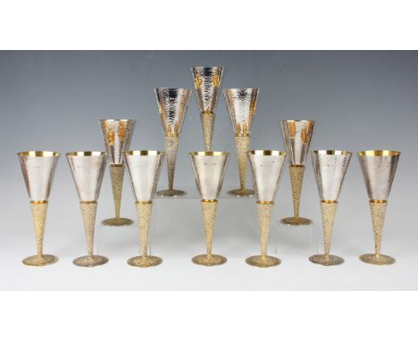 A set of twelve Elizabeth II Stuart Devlin modernist silver and silver gilt champagne flutes, each spot-hammered tapering bow