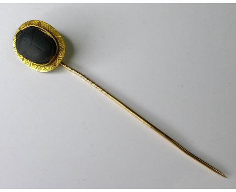 A yellow metal stick pin inset with a ceramic scarab beetle, tests as 22ct gold, 8cm long, 3.8g, with original fitted case. 