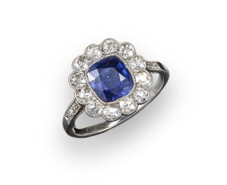 A sapphire and diamond cluster ring, the cushion-shaped sapphire millegrain-set within a surround of twelve old circular-cut 