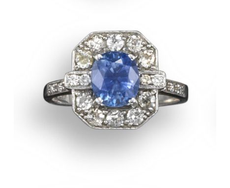 A sapphire and diamond cluster ring, the oval-shaped sapphire is set within a surround of circular-cut diamonds and further d