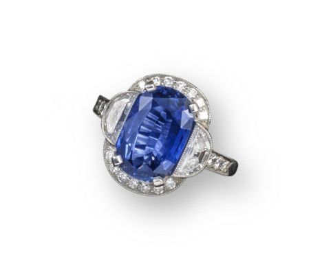 A sapphire and diamond cluster ring, the cushion-shaped sapphire is set within semi-circular shoulder diamonds, millegrain-se