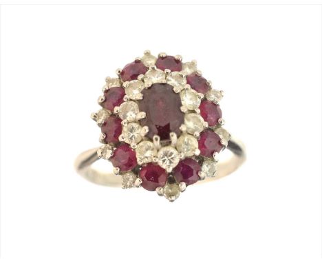 A ruby and diamond cluster ring, the oval shape ruby within a tiered brilliant cut diamond and circular shape ruby surround, 