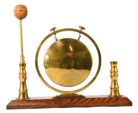 An early 20thC table top brass gong, the central gong on a stepped support, with two candlestick ends, on an oak base, with b