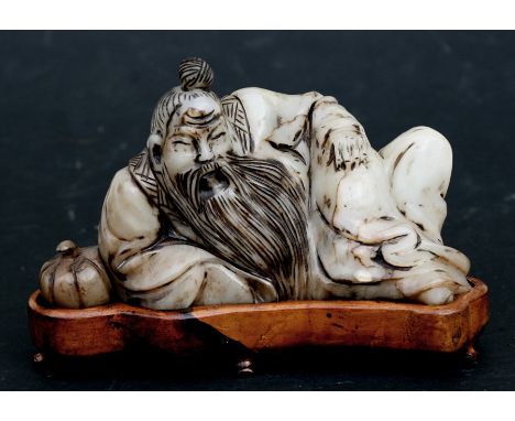 A Chinese jade carving in the form of a recumbent scholar, on a hardwood stand, 15cms (6ins)  wide.