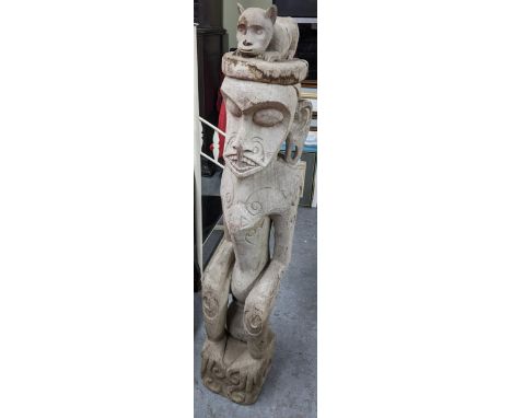 A hardwood carved tribal figure depicted with stylised facial features and incised scrollwork, surmounted by a cat to the top