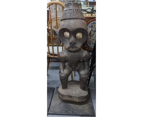 A hardwood carved tribal figure in a crouching posture with inset eyes and on a metal display base, 95cm h Location:If there 