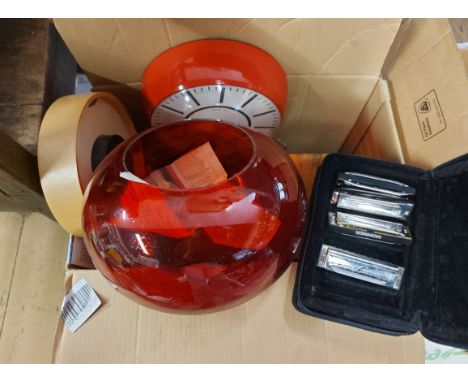 A box containing two modern wall clocks, a soft case with four Hohner harmonicas, a lidded wooden box, large red glass bowl, 
