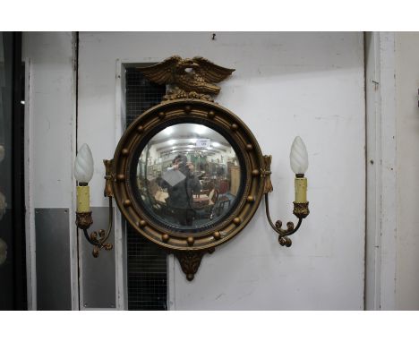 A REGENCY STYLE GILT FRAMED CIRCULAR CONVEX GIRANDOLE MIRROR with eagle crest and two scrolling lamp arms, 46cm wide x 63cm h