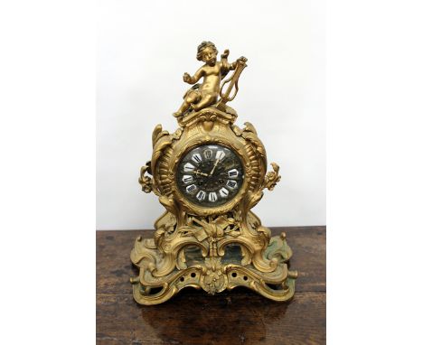 A FRENCH GILT METAL TIMEPIECE the scrolling case surmounted with Putti playing a lyre, the brass dial with white enamel inset