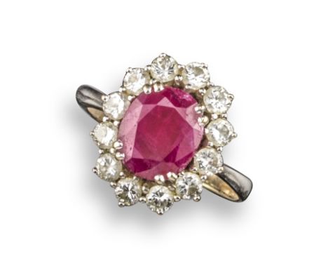 A ruby and diamond cluster ring, the oval-shaped ruby is set within a surround of round brilliant-cut diamonds in white gold,