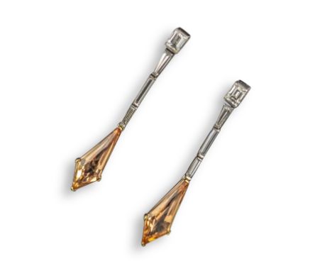 A pair of topaz and diamond drop earrings, the kite-shaped orange topaz suspend from a line of baguette and tapered baguette-