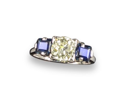 A sapphire and diamond three-stone ring, centred with an old circular-cut diamond between square-shaped sapphires in platinum