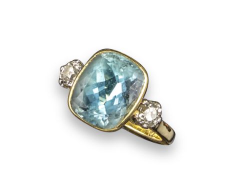 An aquamarine and diamond three stone ring, the cushion-shaped aquamarine is rubover set in yellow gold and flanked with circ