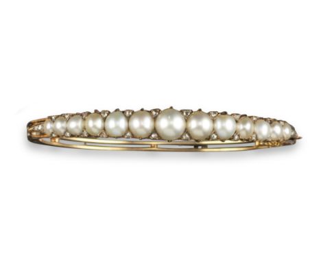 A Victorian pearl and diamond bangle, the half pearls set with diamond pointers in carved and pierced yellow gold mount. 5.7c