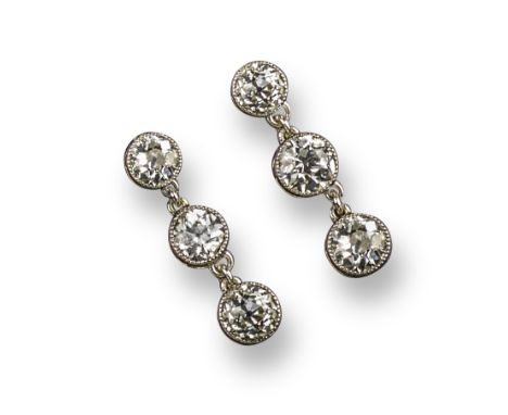 A pair of diamond drop earrings, set with three old circular-cut diamonds in articulated platinum and gold rubover mounts, po