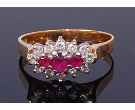 An 18ct gold, ruby and diamond dress ring, arranged as a raised row of three round cut rubies in a surround of twelve small b