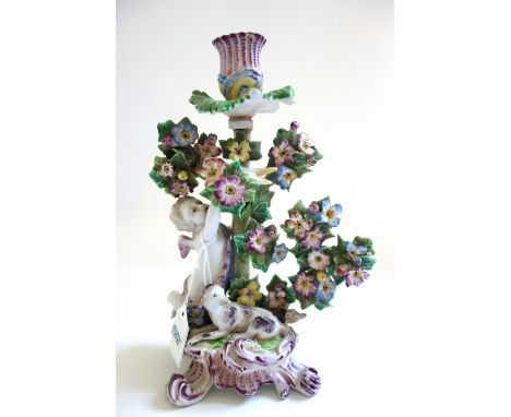 A Bow candlestick group, circa 1765, modelled as Cupid reaching up towards a bird perched in flowering branches, a recumbent 