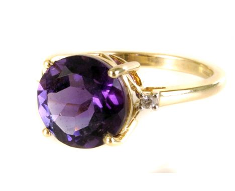 A 9ct gold amethyst and diamond three stone ring, the large round cut amethyst in tall four claw setting, flanked by two smal