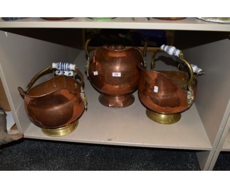 Three copper and brass coal helmets, two having patterned ceramic handles and the other wooden handles.