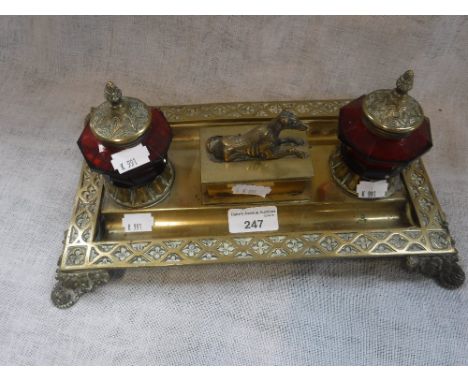 A 19TH CENTURY BRASS INKSTAND, the box lid decorated with a whippet with cut ruby glass inkwells, 31 cm wide