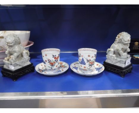 A PAIR OF CHINESE HARDSTONE LIONS on wooden bases and a pair of Oriental ceramic beakers with saucers