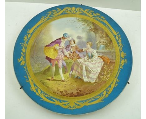 A SEVRES STYLE CERAMIC WALL PLATE having gilded blue ground rim, to the centre a scene of lovers in 18th Century costume in a